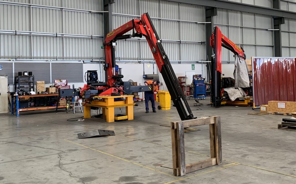 Technician working on a red Palfinger crane mounted on a stand in a workshop.